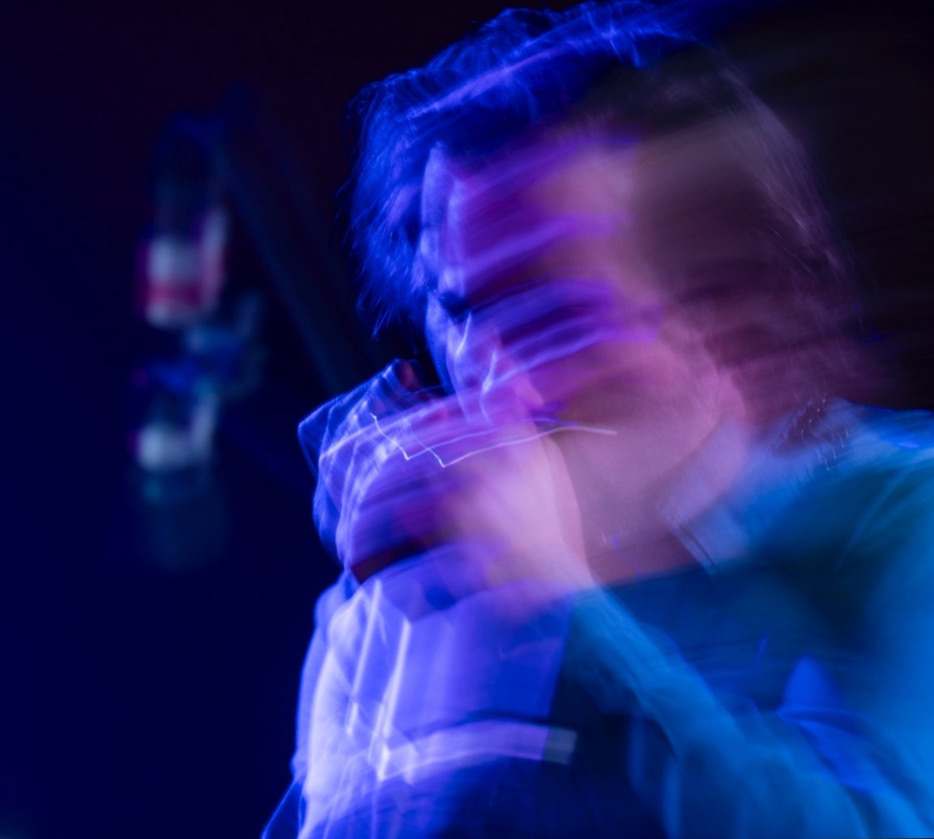 A long-exposure blur of Willy B playing harmonica in blue and violet light